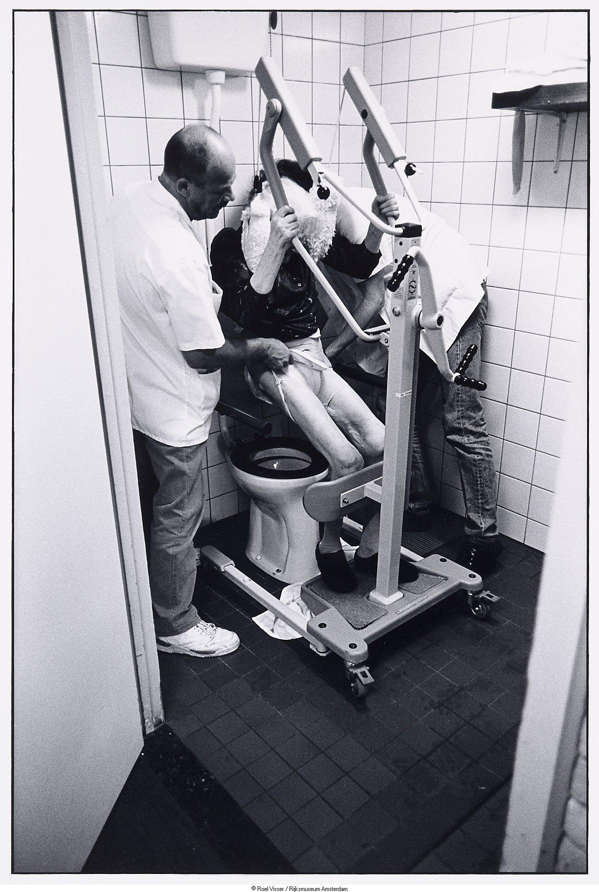 Een geestelijk zieke bejaarde wordt geholpen op het Toilet - Amsterdam