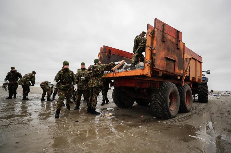 De rommel wordt in een kiepwagen gegooid die achter een tractor hangt. Deze rijdt mee met de schoonmakende militairen. (foto: Ministerie van Defensie)