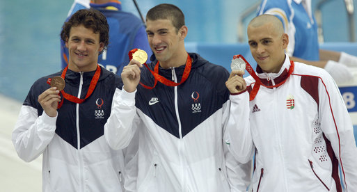 Michael Phelps (midden) met één van zijn vele olympische gouden medailles (WikiCommons/White House photo by Eric Draper)